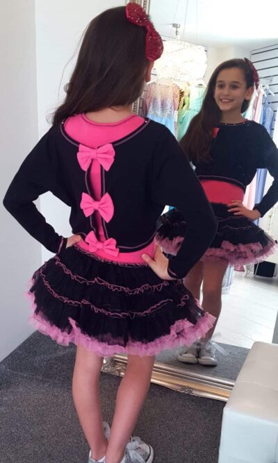 Young girl wearing Ooh la la Couture fabulous jersey crop top with gorgeous hot pink stitching and hot pink bows on the back over a jersey bodice and black & hot pink tutu skirt from a Girls Party Dress Specialist Boutique