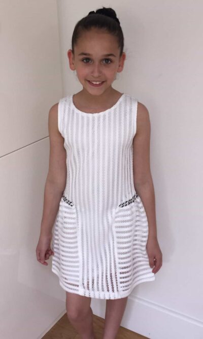 Young girl wearing Ivory skater style dress with side chain detail in ladder mesh like fabric from Party Dress Boutique, Silhouette London