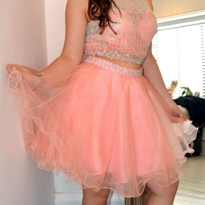 Teenage model wearing a Blush Prom Dress Style 89 in coral. Two piece that features a completely encrusted jewel neckline and top, matching beaded waist, and chiffon skirt from Silhouette London, Girls party dress specialists in London.