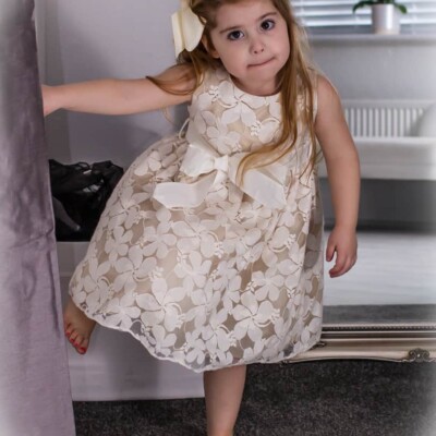 Young Girl wearing an Ivory Jasmine Lace dress with matchingbow belt at the waistband from Silhouette London a Girls Party Dress Specialist in Greater London