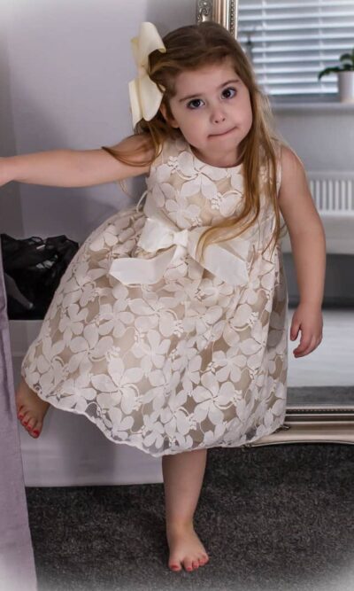 Young Girl wearing an Ivory Jasmine Lace dress with matchingbow belt at the waistband from Silhouette London a Girls Party Dress Specialist in Greater London